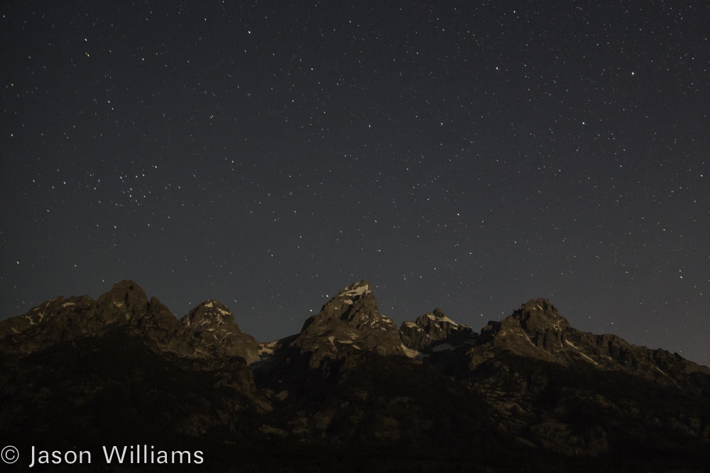 Stars and Constellations Appear In The Night Sky Above The Grand Teton Range