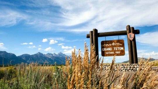 Pictured Is The Welcome To Grand Teton Sign With A View Of The Grand Tetons In The Distance