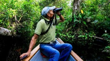 man using binoculars in canoe in the amazon