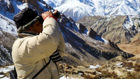 man using binoculars to view the himalayas