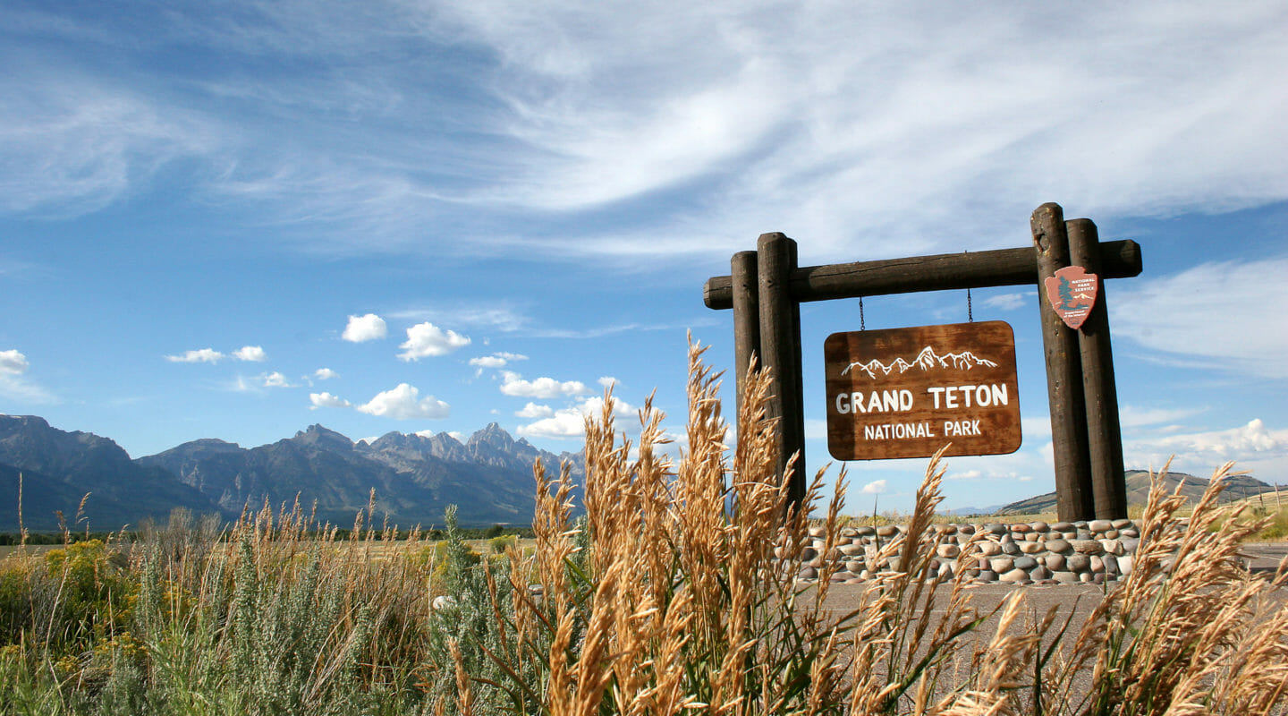 The Wooden Sign For Grand Teton National Park Marks The Park Boundary With The Grand Teton Range Visible In The Distance