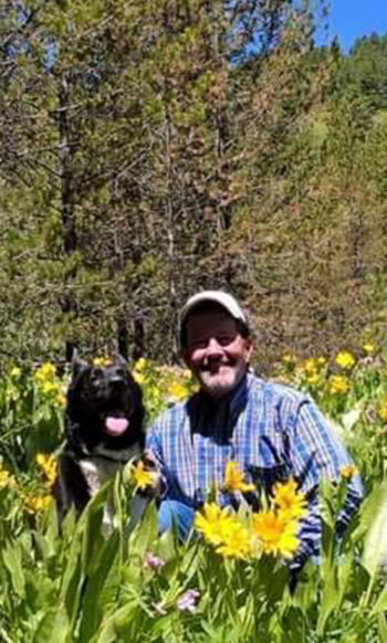 Jeffrey Meehan Poses In A Field of Arrowleaf Balsamroot With His Dog In The Greater Yellowstone Ecosystem